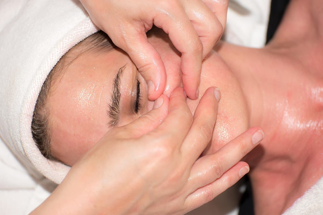 A client lying back with eyes closed while a therapist works on her face